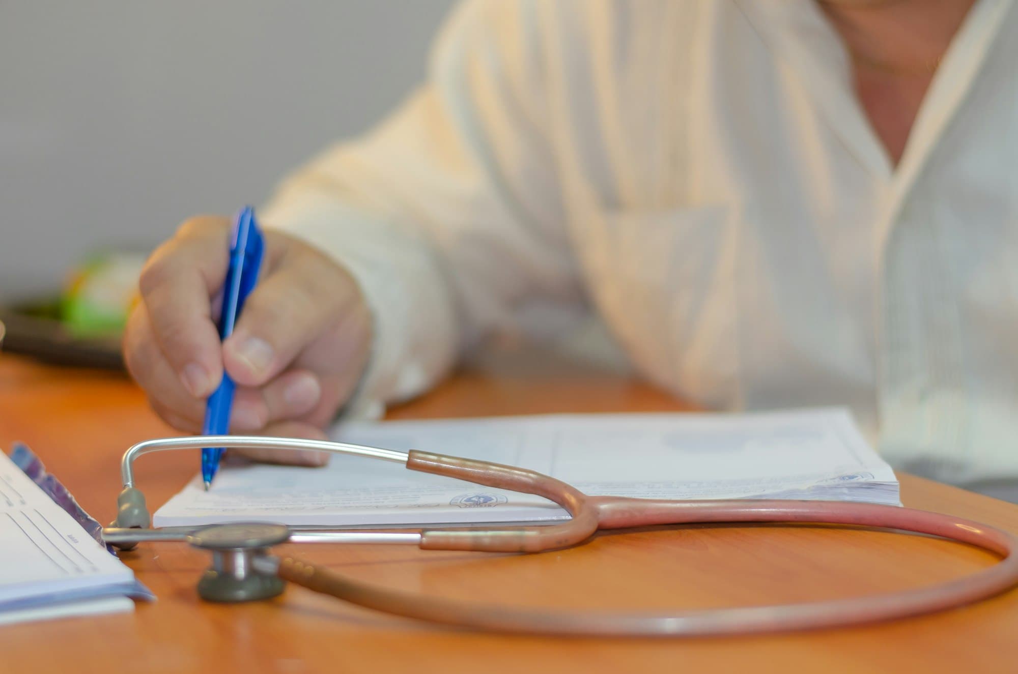 Médico preenchendo um documento com um estetoscópio sobre a mesa