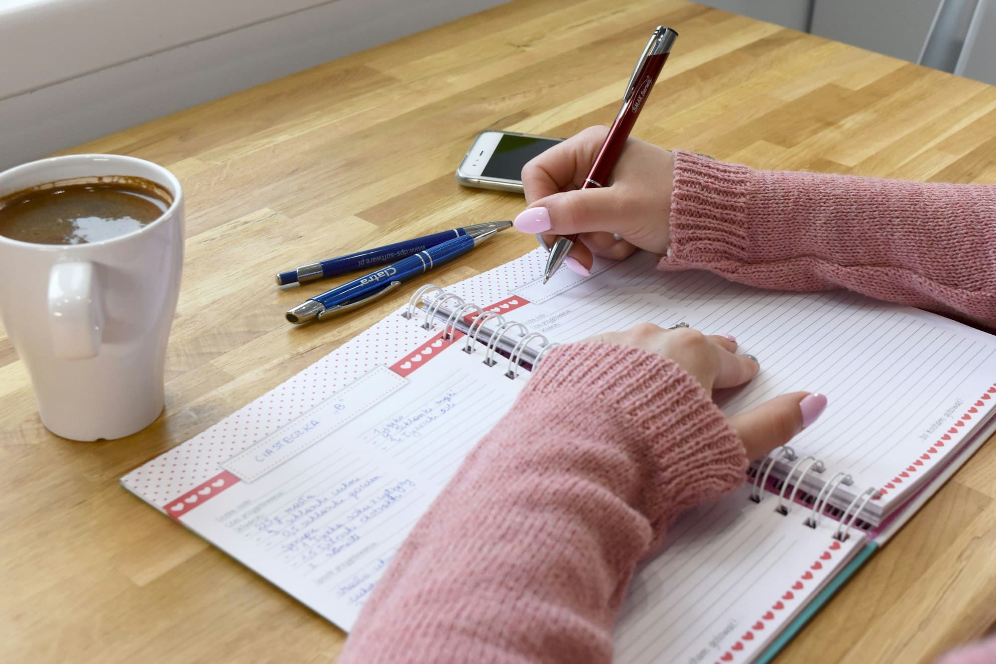 Mãos anotando num caderno ao lado de uma xícara de café